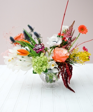 This centerpiece style arrangement includes a diverse array of textured blooms with warm tones.